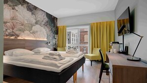 A modern hotel room with a large bed, a desk, a chair, a television, and a view of a building through a window. - Thon Hotel Saga (Haugesund)