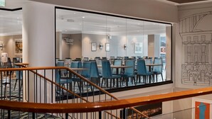 A hotel dining area with glass walls, blue chairs, and a staircase with wooden railings. - Thon Hotel Saga (Haugesund)