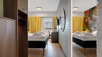 A modern hotel room with two beds, a large mirror, and a view of a construction site through the window.