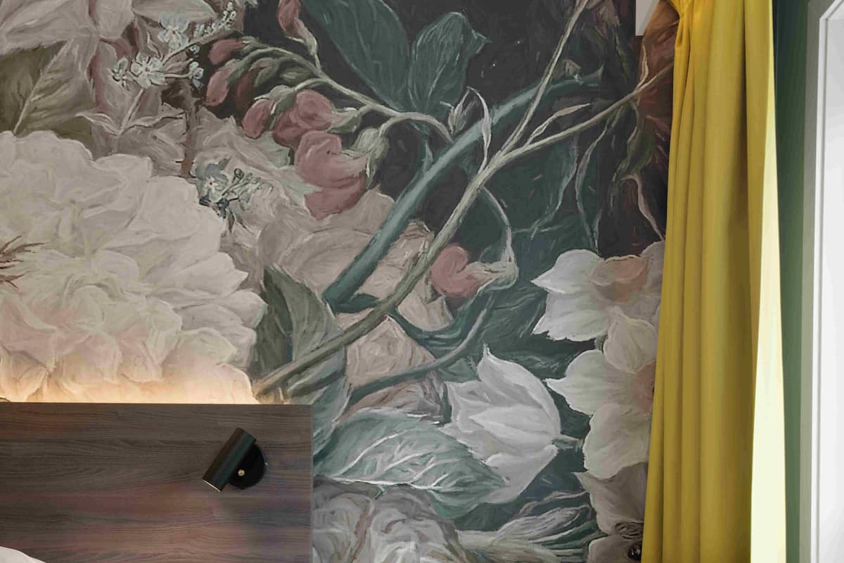 A modern room with a large floral mural, a yellow armchair, a wooden nightstand, and a round table.