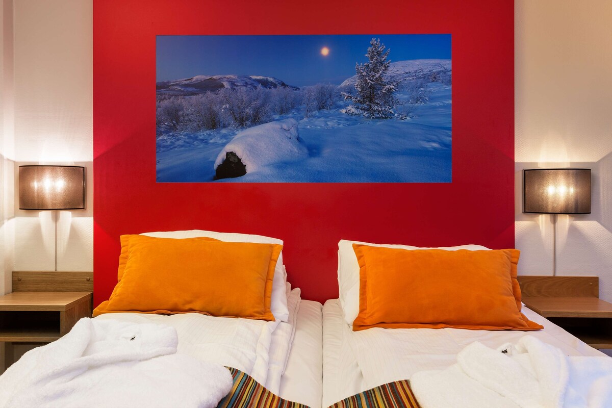 A hotel room with two beds, red walls, and a large picture of a snowy landscape.