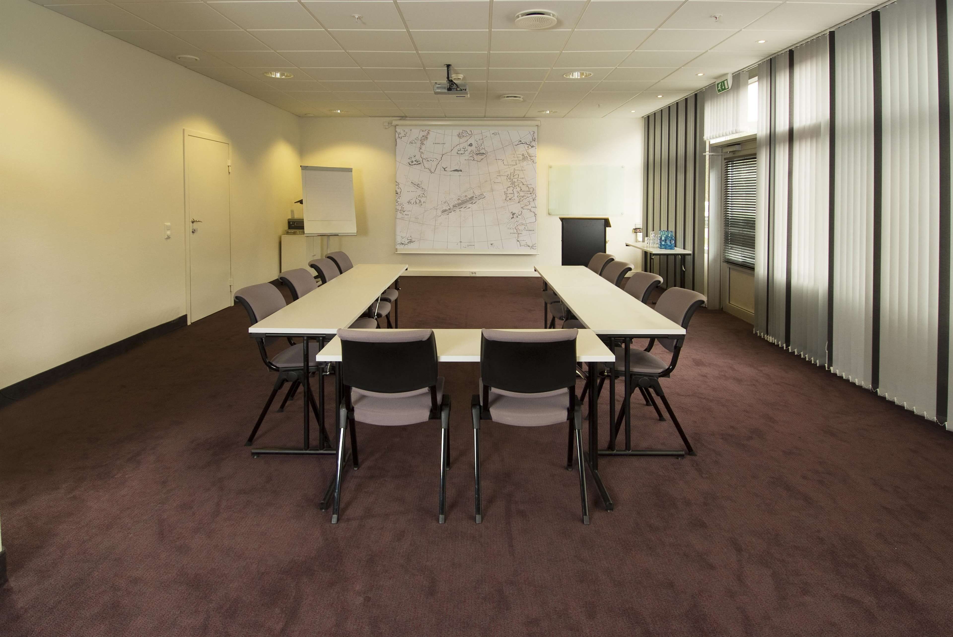 Een vergaderruimte met een grote tafel, stoelen, een beamer, een whiteboard en een kaart aan de muur.