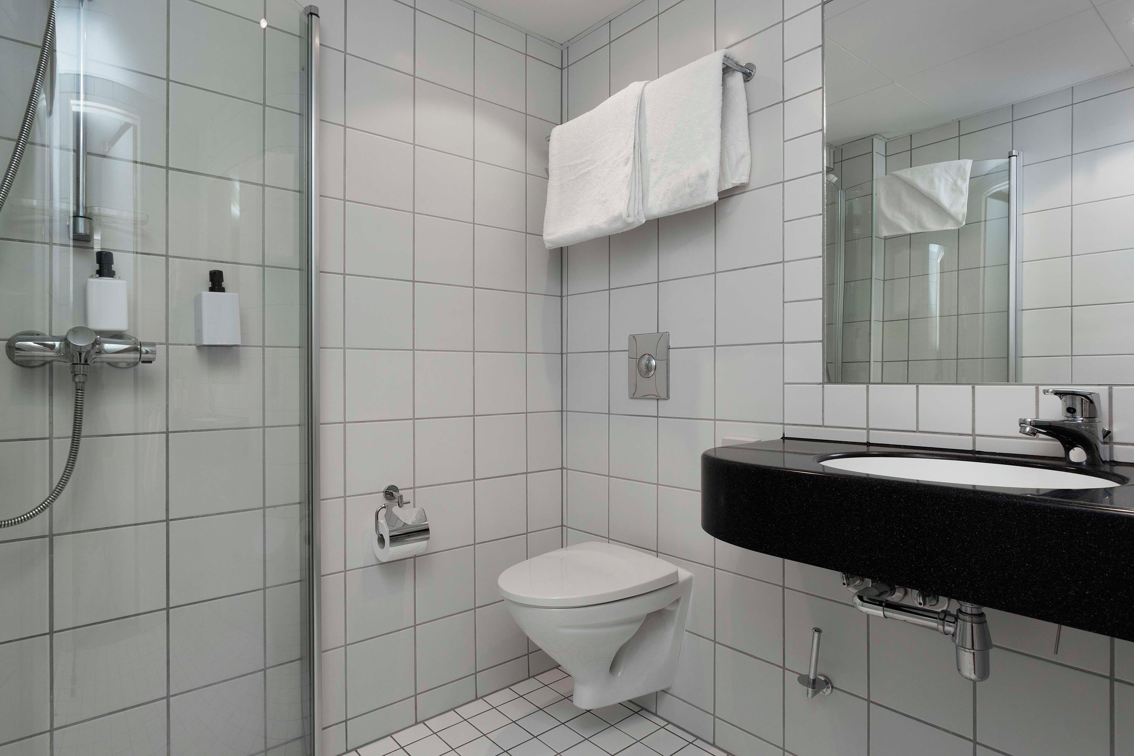 A modern bathroom with a glass shower enclosure, a white toilet, and a black sink with a mirror above it.