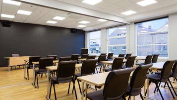 Ein Klassenzimmer mit Reihen von Schreibtischen und Stühlen, großen Fenstern und einem Projektor an der Decke.