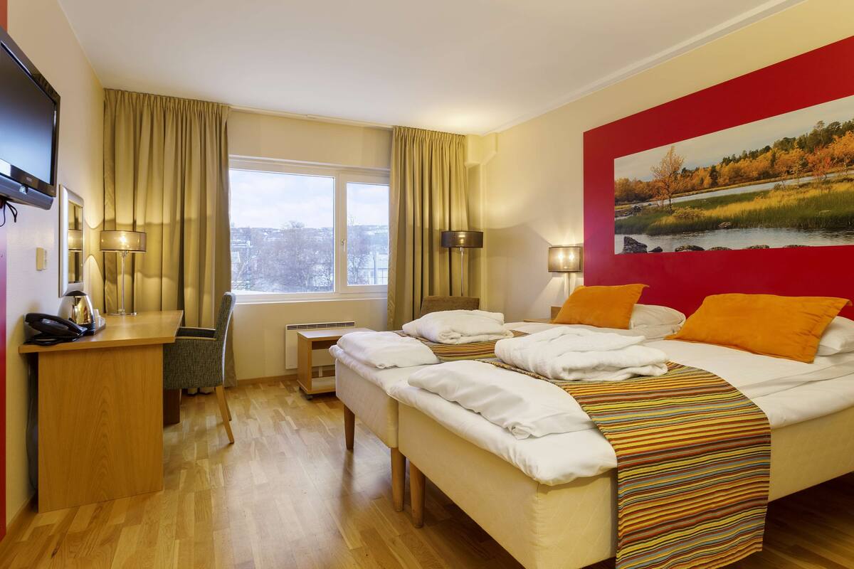 Habitación de hotel con cama, escritorio, silla, televisor y un cuadro en la pared.