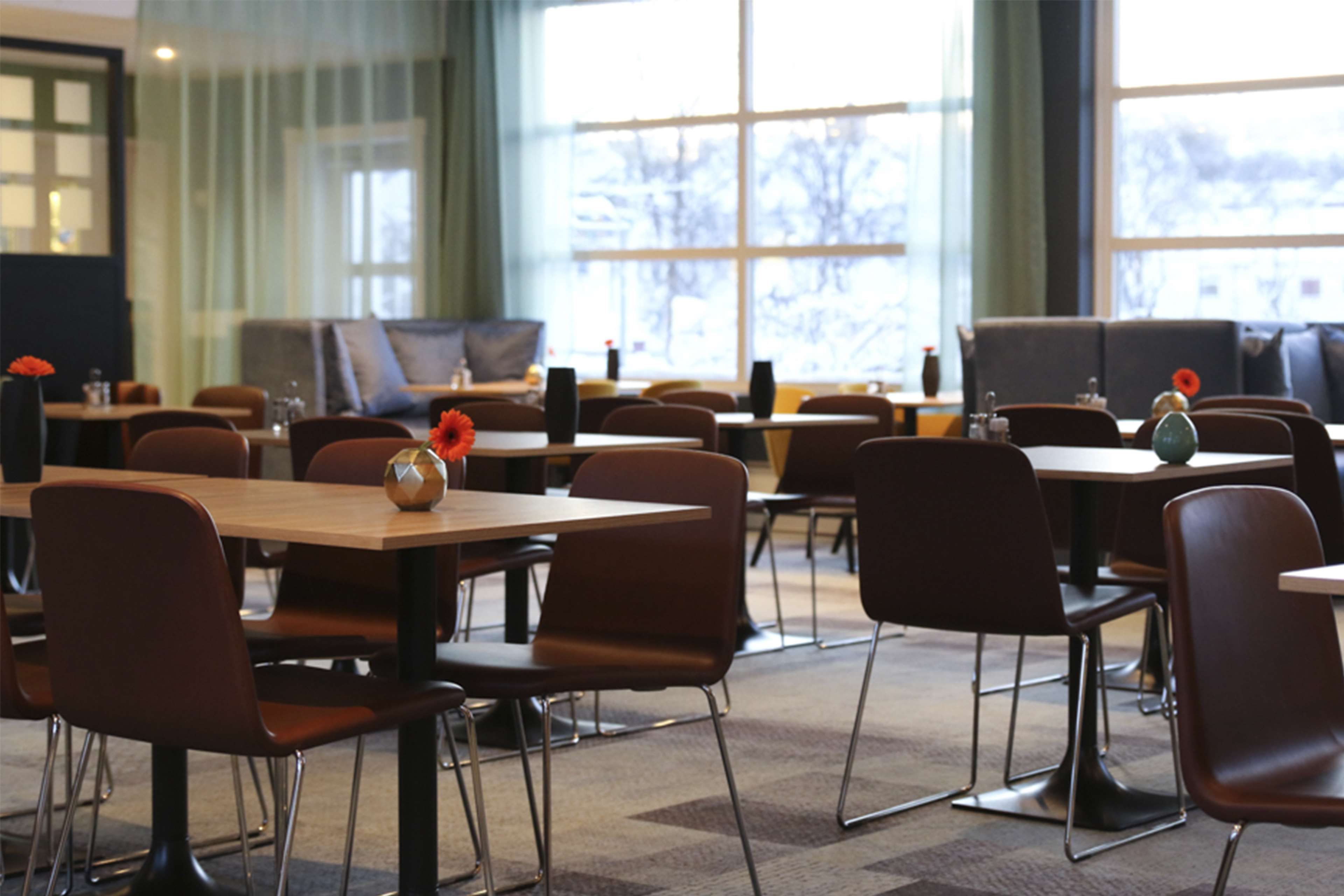 A spacious dining area with multiple tables and chairs, large windows with a view of trees, and a modern interior design.