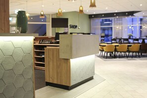 A modern reception area with a wooden counter, hexagonal patterned wall, and yellow chairs. - Scandic Kirkenes (South Varanger)