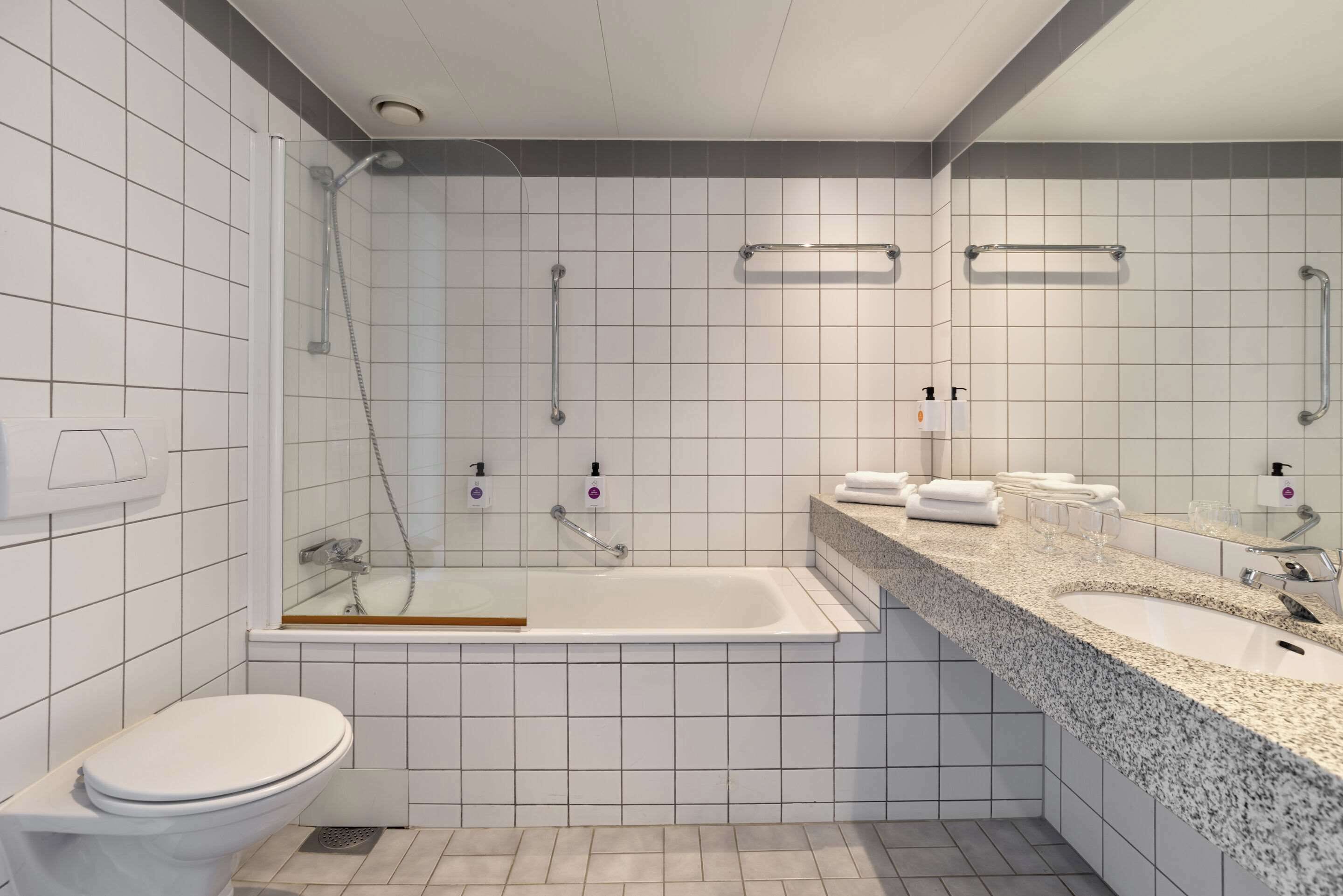 Une salle de bain moderne avec des toilettes blanches, une douche à parois de verre, une baignoire et un comptoir en granit avec un lavabo et un miroir.