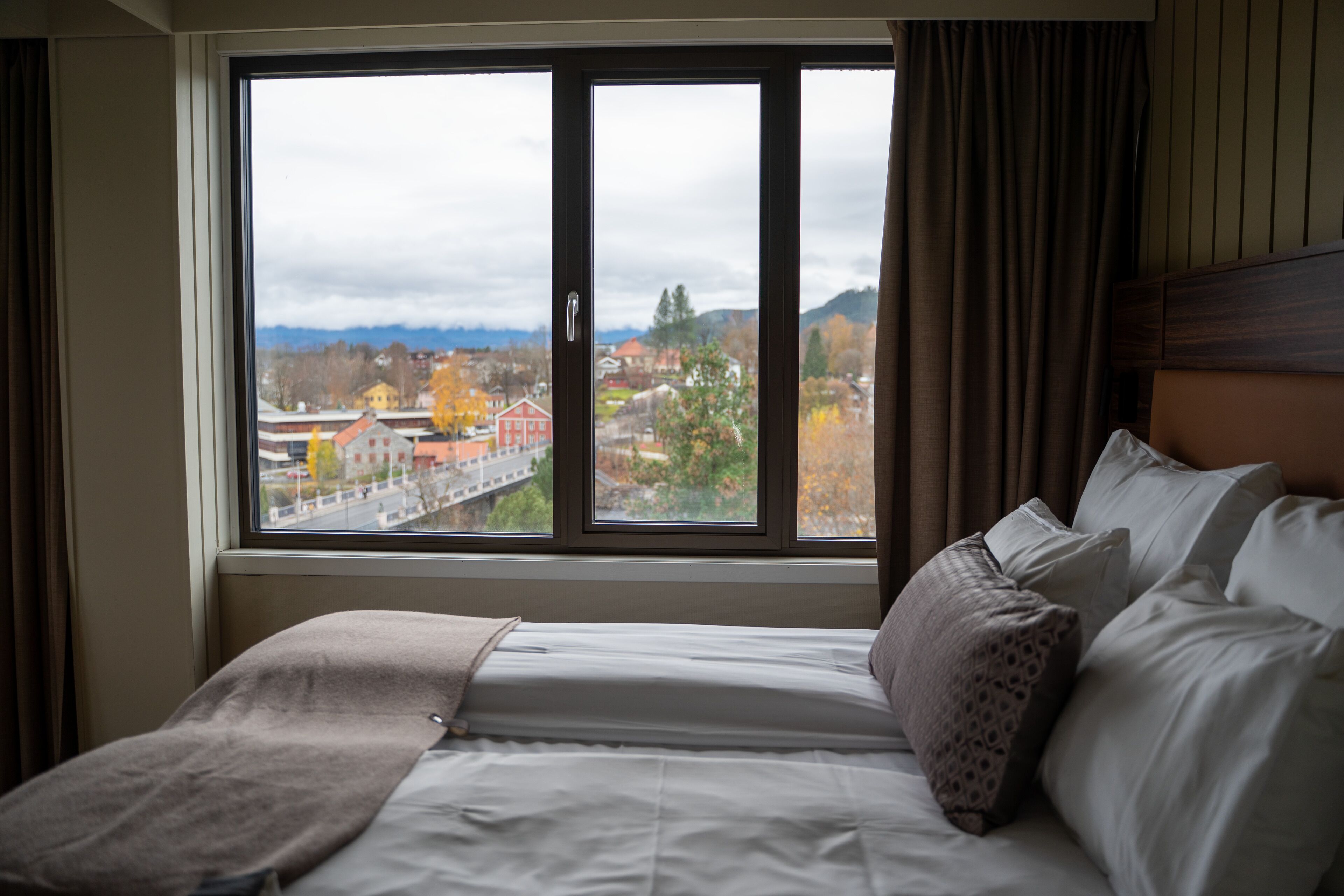 Quarto de hotel com uma grande janela que oferece vista para uma cidade e montanhas.