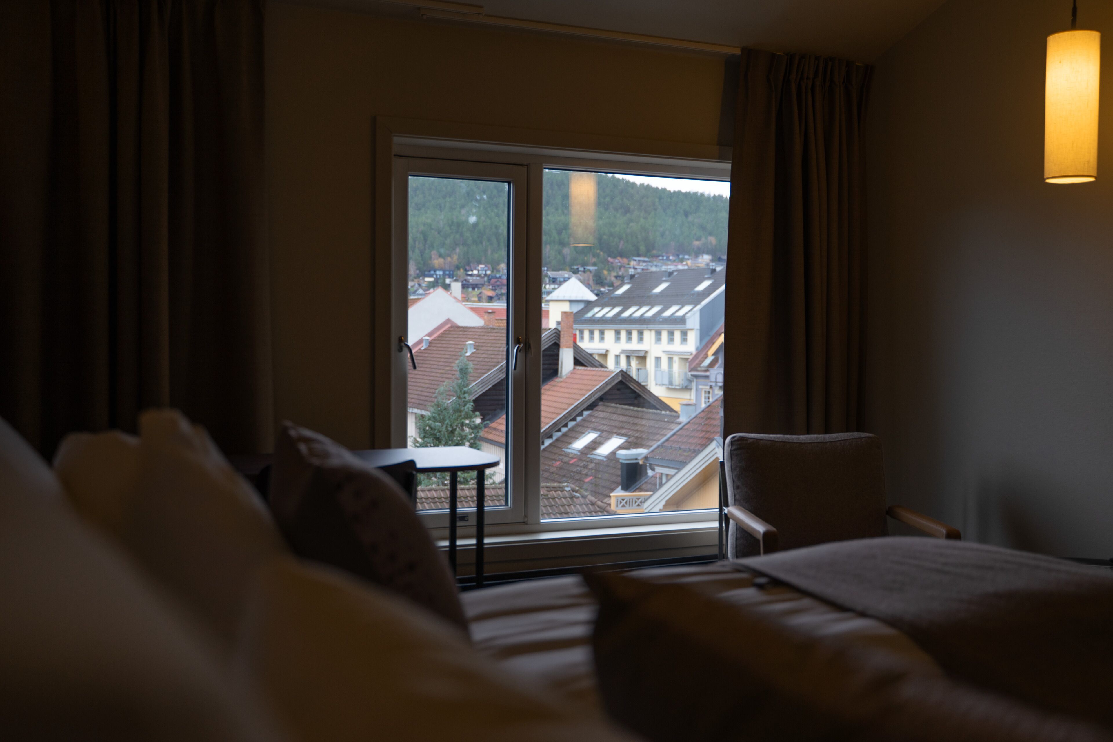 A hotel room with a large window, a bed, a chair, and a table.