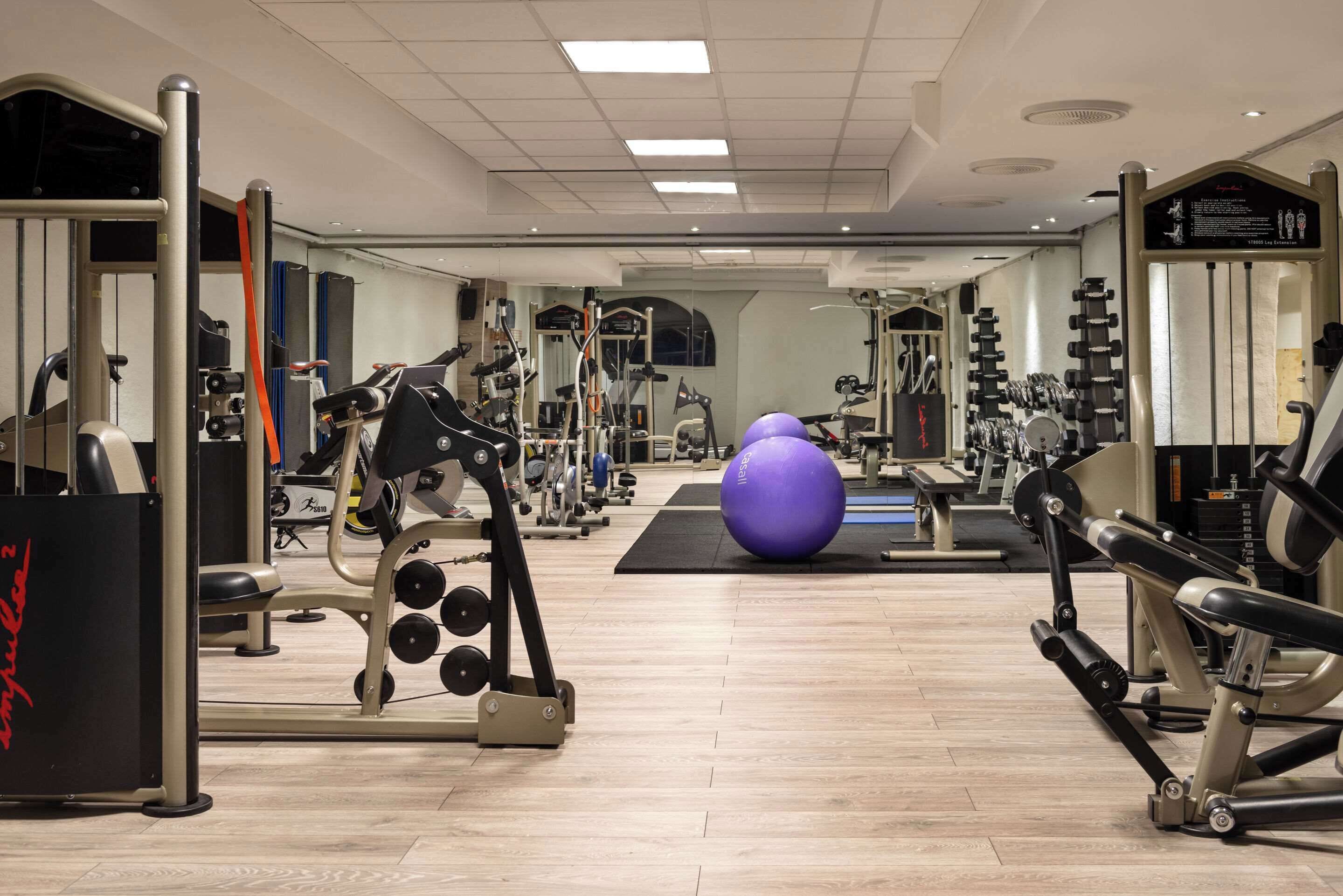 Een fitnessruimte met diverse trainingsapparaten, waaronder een bankdrukpers, gewichten en een grote fitnessbal.