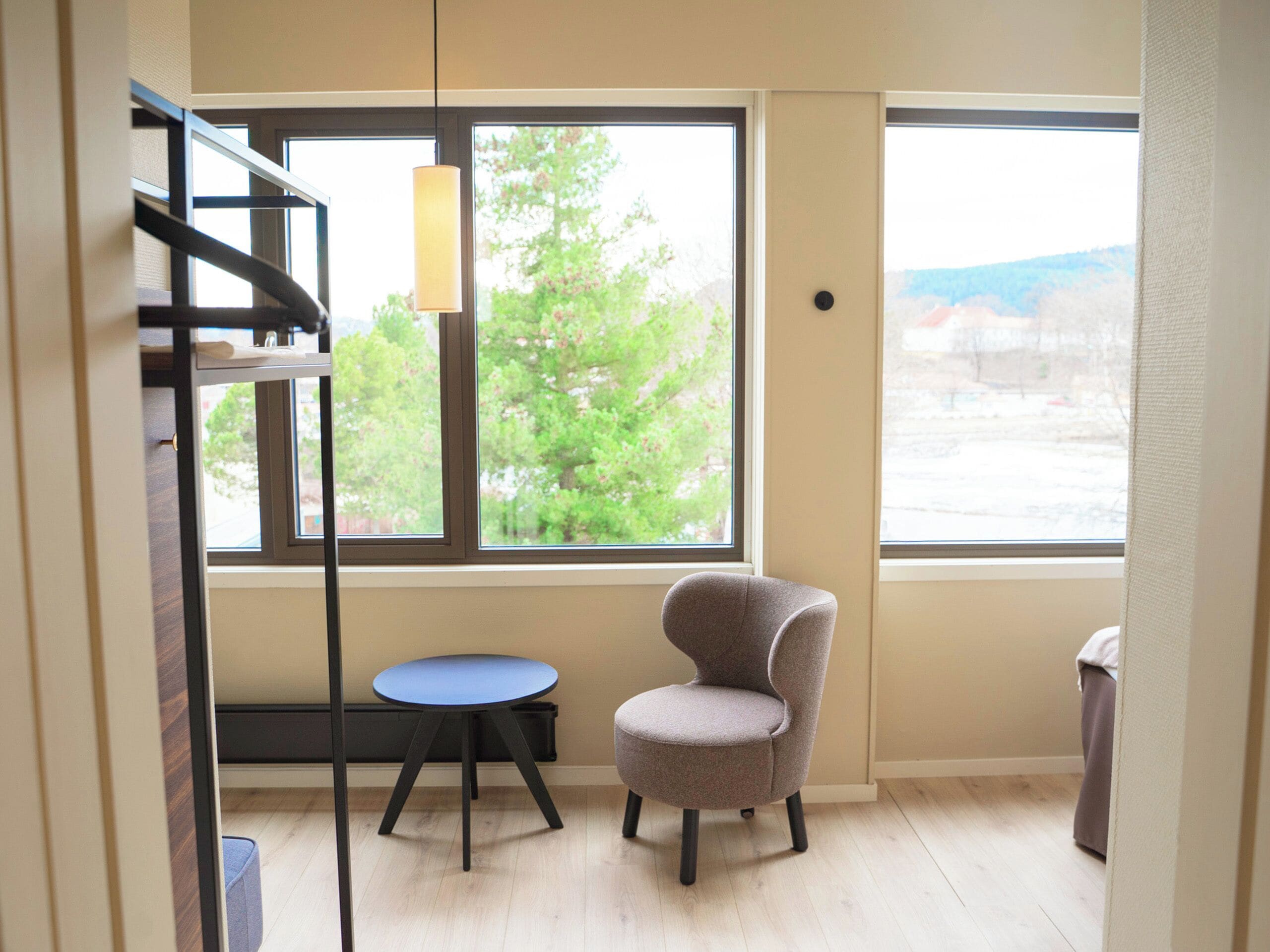 A room with a large window, a chair, a small table, and a hanging light fixture.