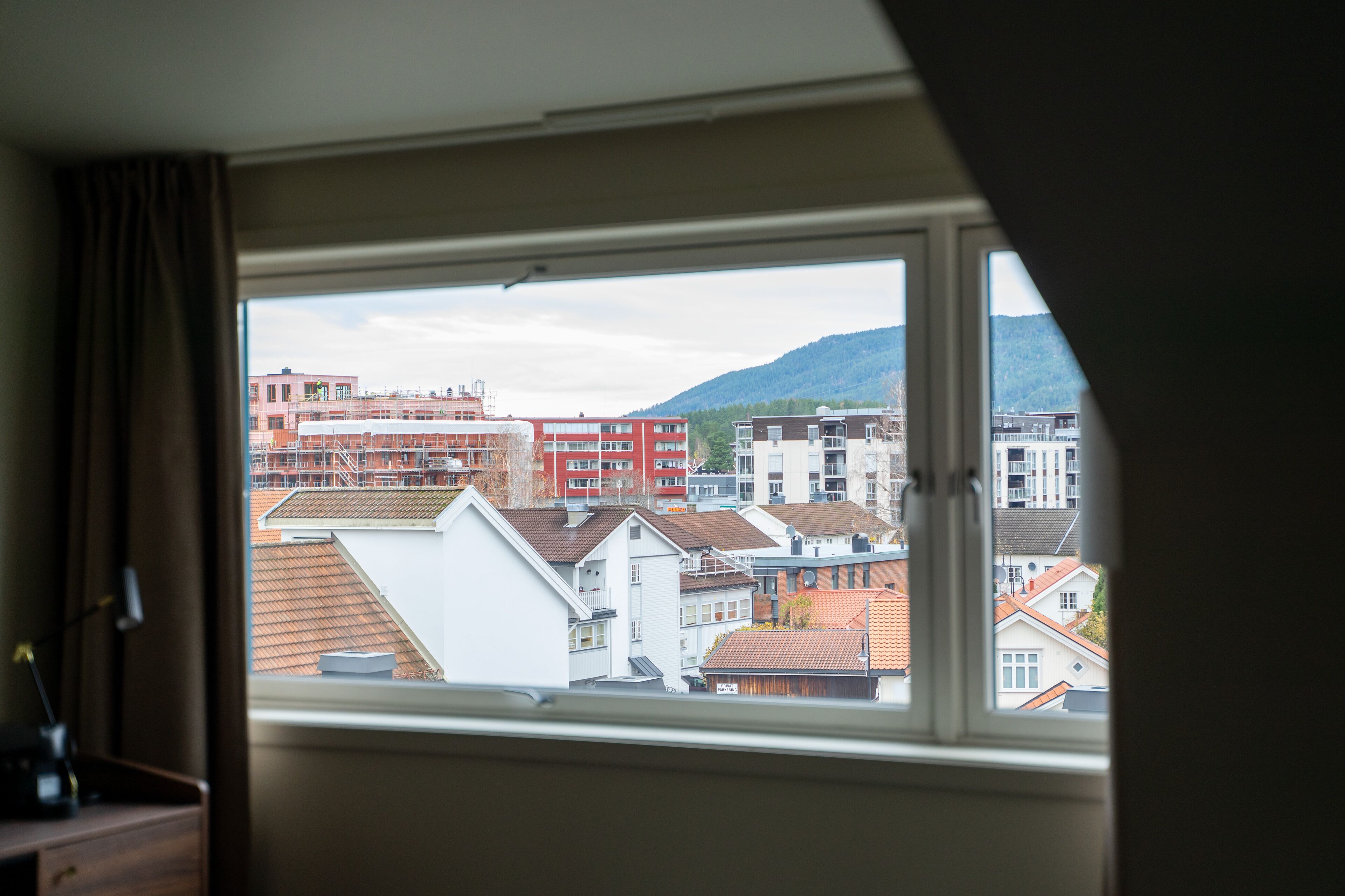 A view from a window overlooking a cityscape with buildings and a hill in the distance.