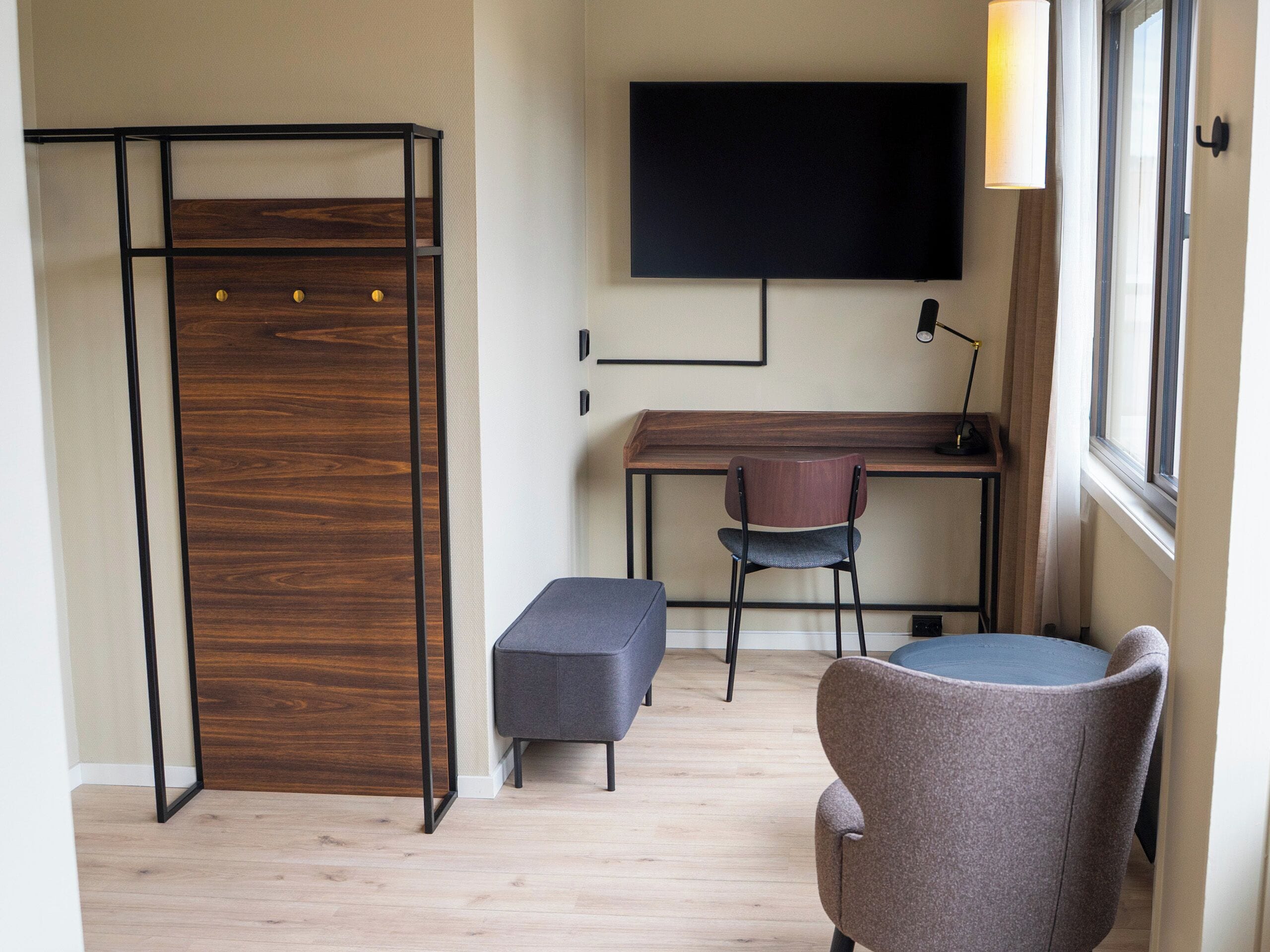 Une pièce comprenant un bureau, deux chaises, un banc, un téléviseur et une fenêtre.