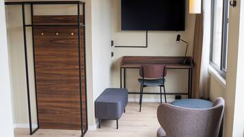 Une pièce comprenant un bureau, deux chaises, un banc, un téléviseur et une fenêtre.