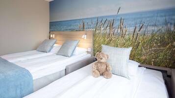 Een hotelkamer met twee bedden, een grote muurschildering van een strand en een teddybeer op een van de bedden.