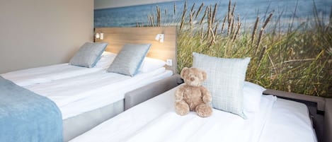 Ein Hotelzimmer mit zwei Betten, einem großen Wandgemälde mit Strandmotiv und einem Teddybären auf einem Bett.
