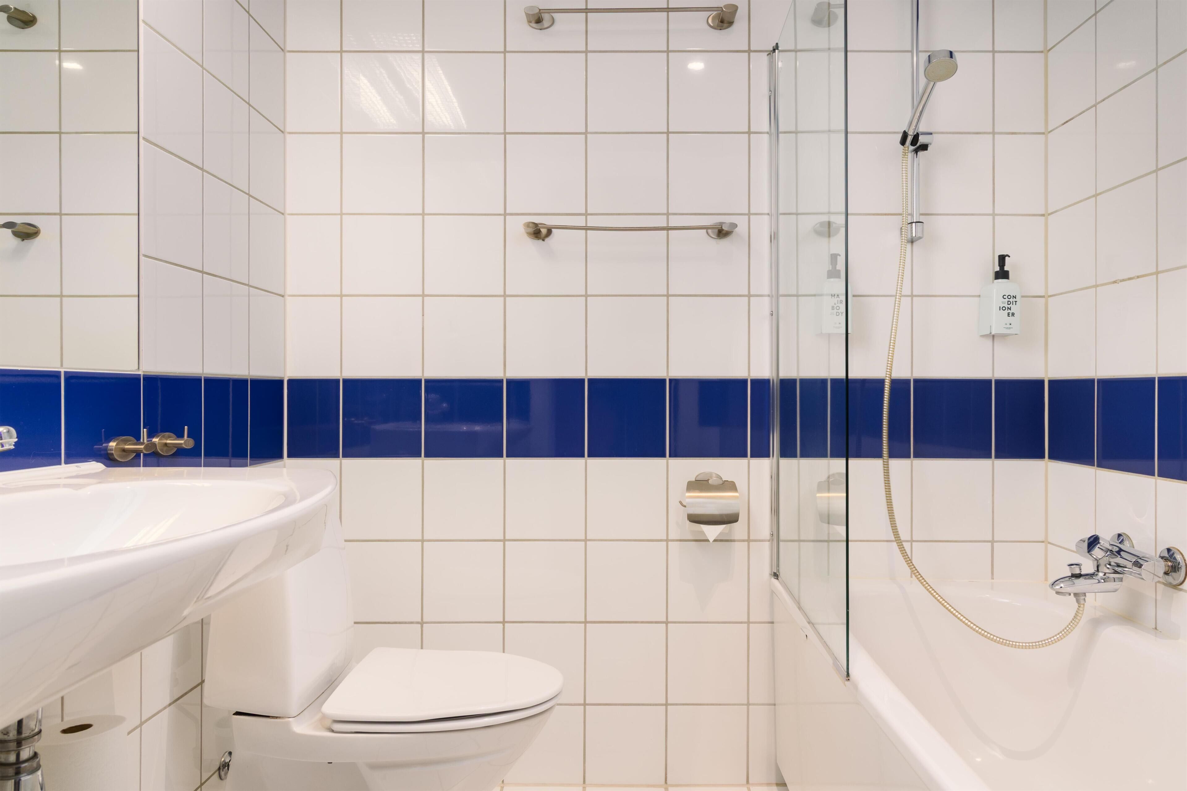 Un bagno con un lavandino, un water e una vasca da bagno bianchi, con piastrelle blu nella parte inferiore della parete.