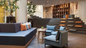 Un vestíbulo moderno con un sofá modular, sillones, una mesita y una escalera adornada con cojines.