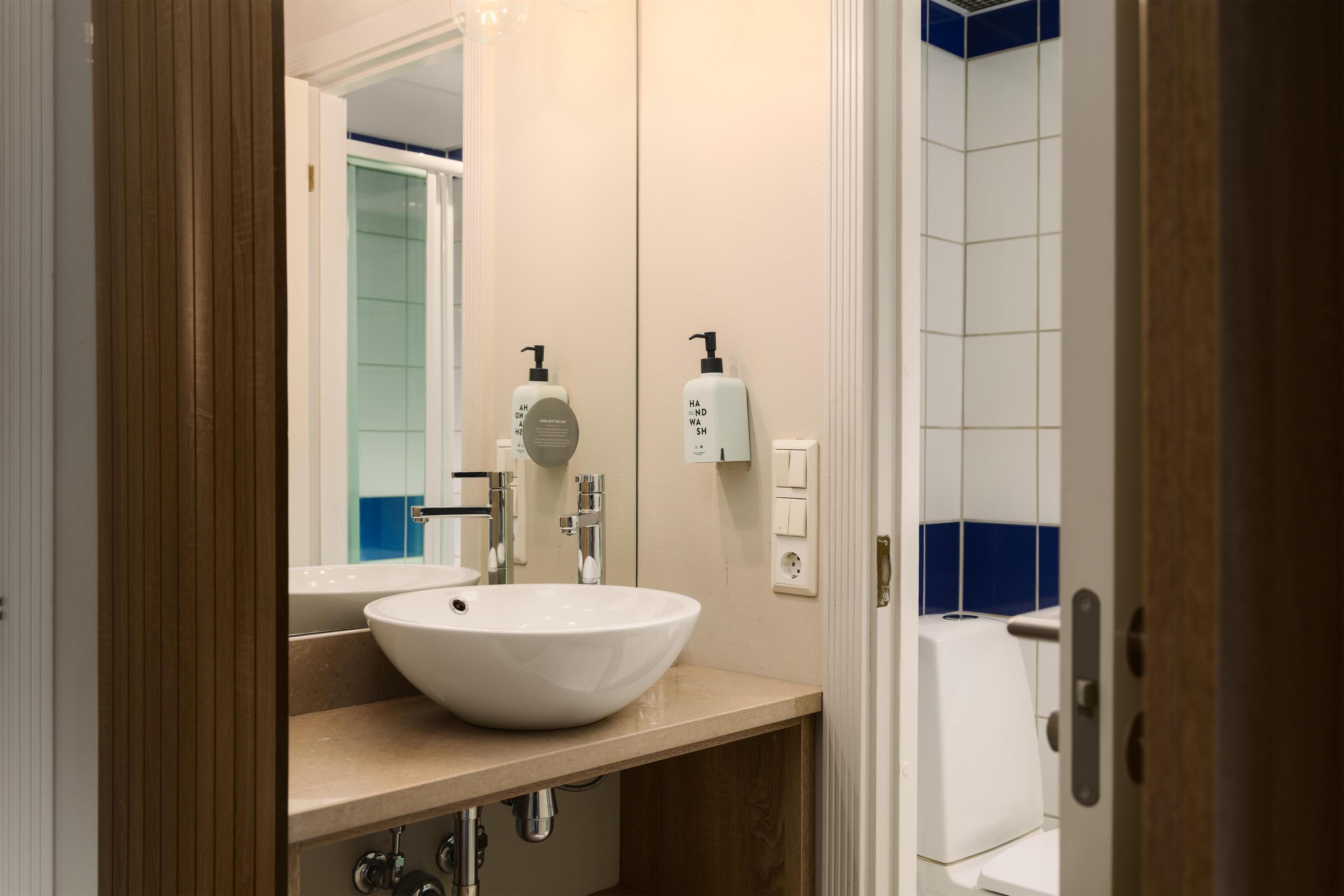 Een badkamer met een witte wastafel, een spiegel, een zeepdispenser en een toilet.