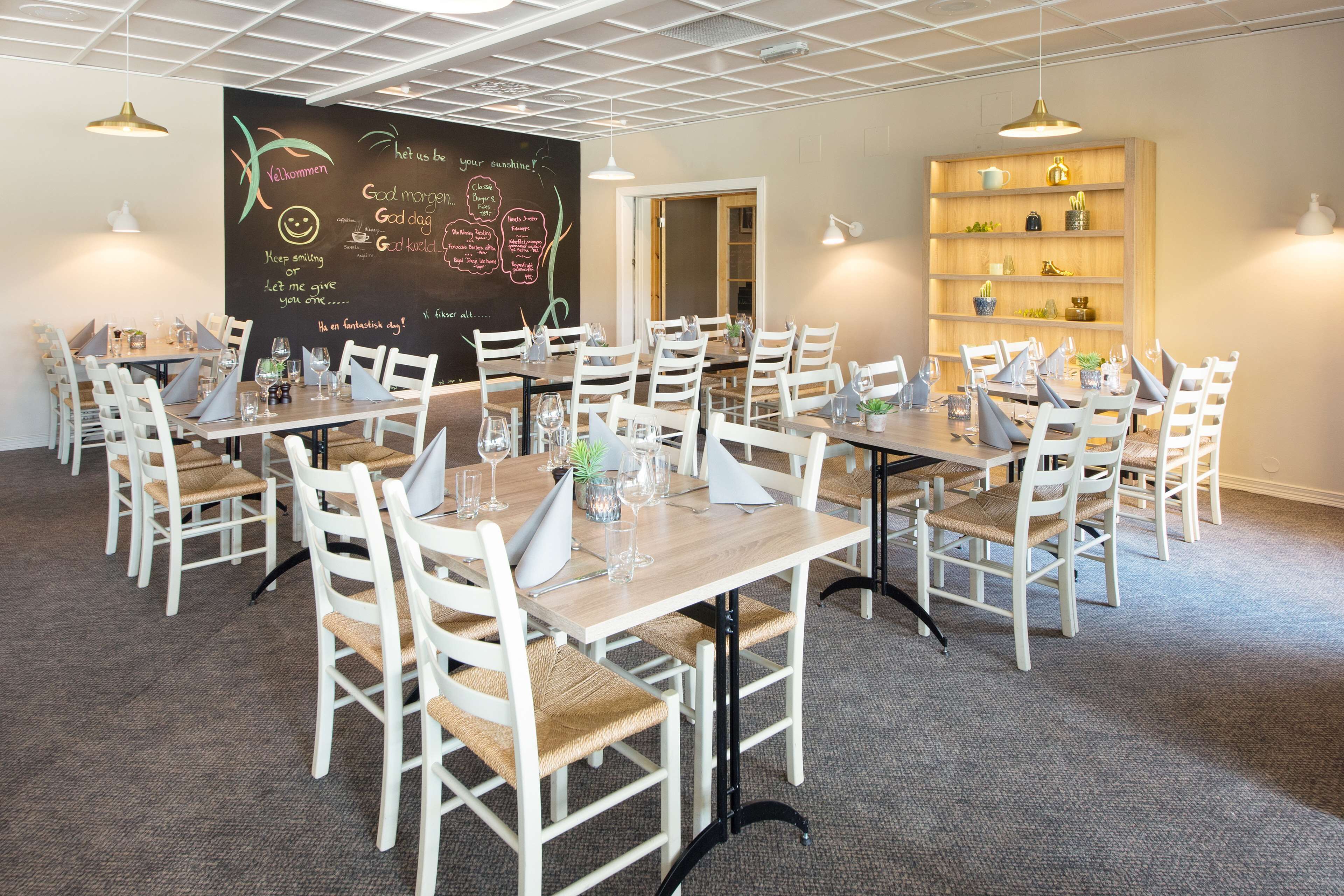 Zona pranzo con diversi tavoli e sedie, una lavagna con frasi motivazionali e uno scaffale con oggetti decorativi.