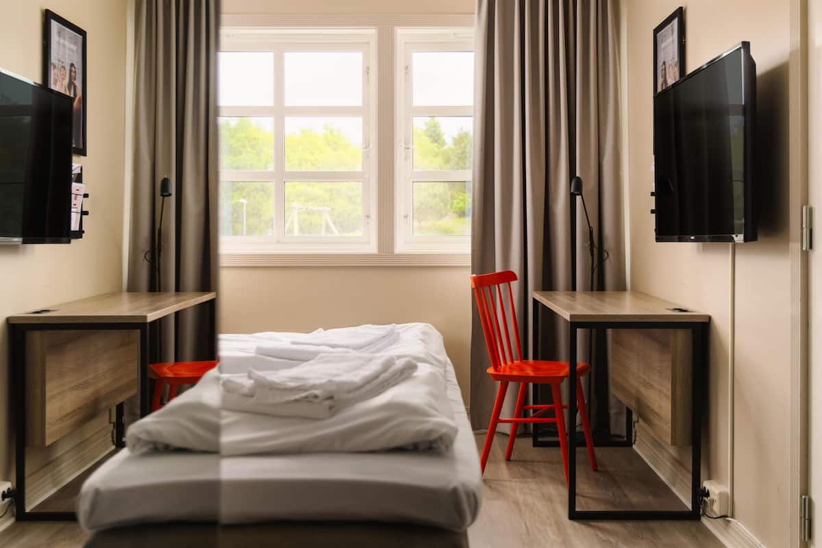 A hotel room with a bed, two desks, a chair, a TV, and a window with curtains.