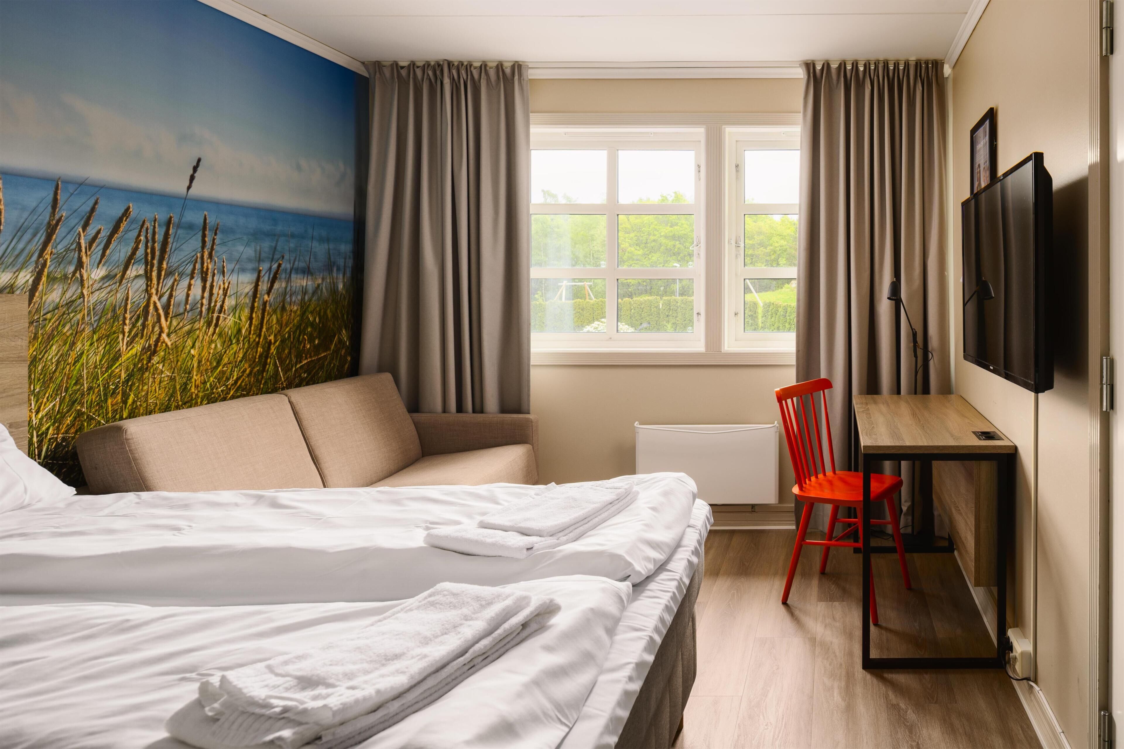A hotel room with a bed, a desk, a chair, a TV, and a window with curtains.