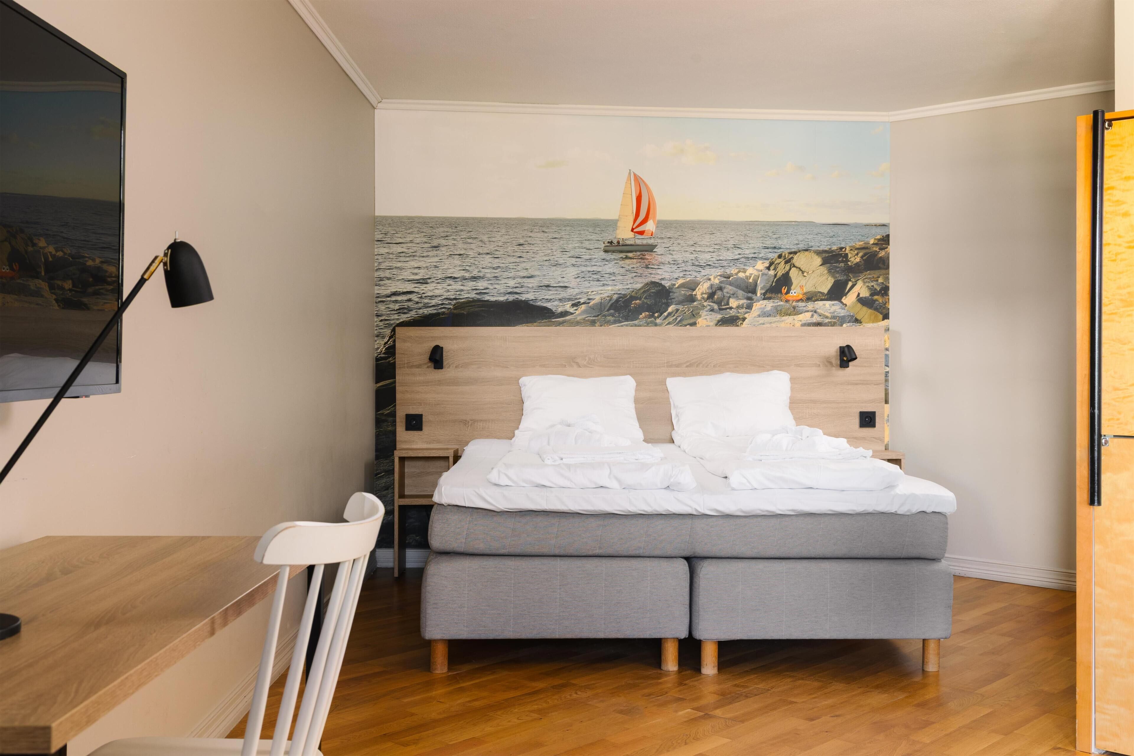 Un dormitorio con cama, escritorio, silla y un mural en la pared de un velero sobre el agua.