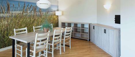 A dining area with a wooden table and chairs, a wall mural of grass, a pendant light, and a built-in cabinet.