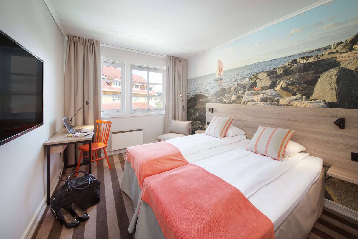 A hotel room with a bed, desk, laptop, chair, and a view of the sea through a window.