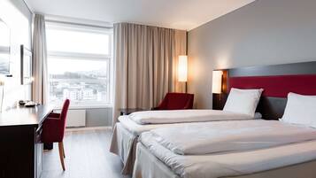 A hotel room with two beds, a desk, a chair, a lamp, and a view of the city.