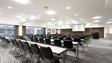 A conference room with rows of tables and chairs, a projector screen, and a podium.