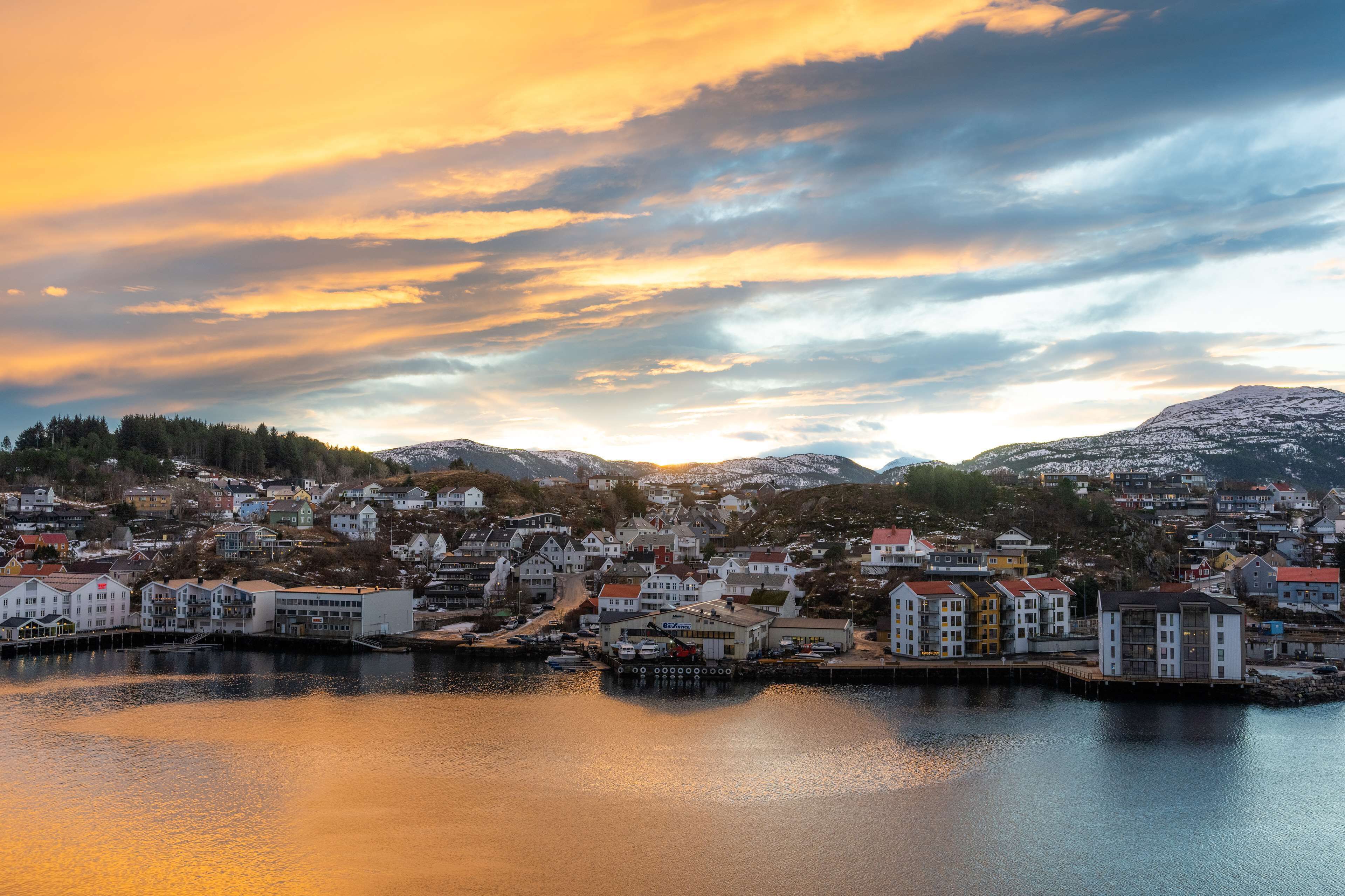 A coastal town with buildings along the waterfront, a dock, and a mountainous backdrop.