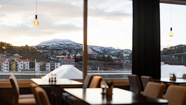Restaurante com mesas e cadeiras, vista para uma montanha nevada e lâmpadas penduradas.