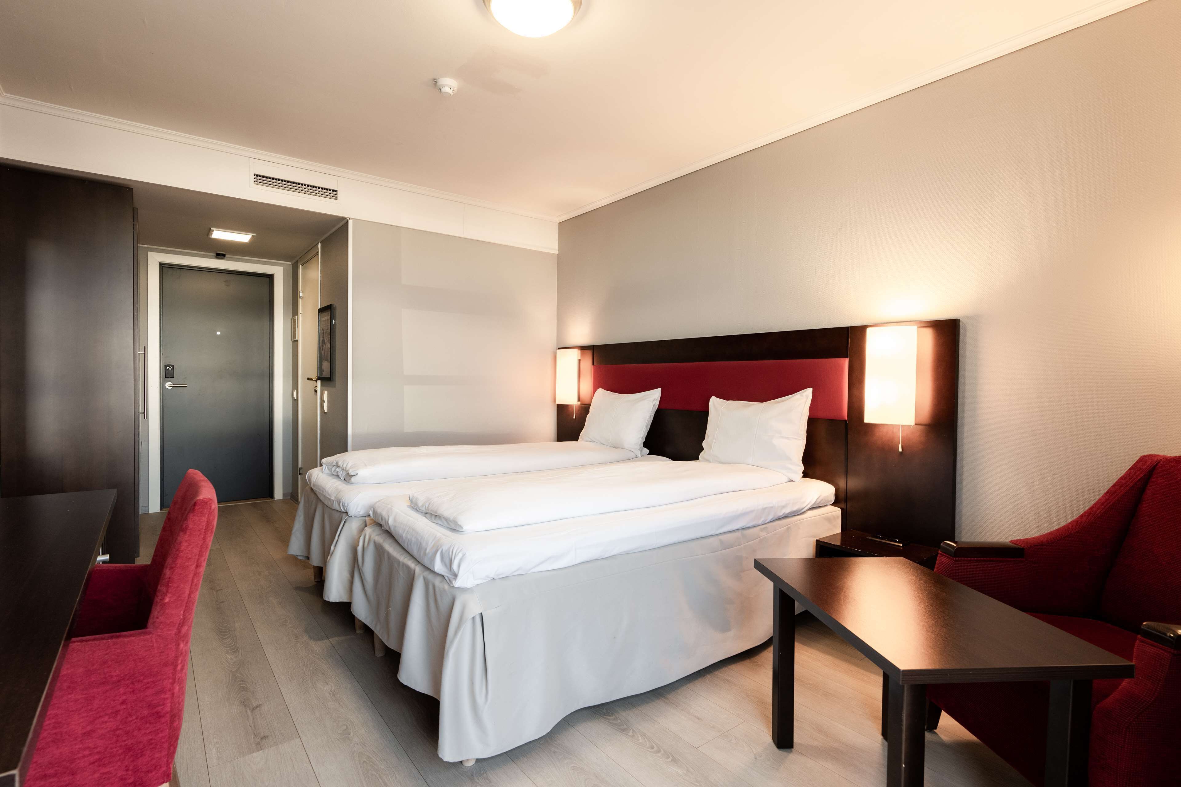 Habitación de hotel con dos camas, un escritorio y un sillón rojo.