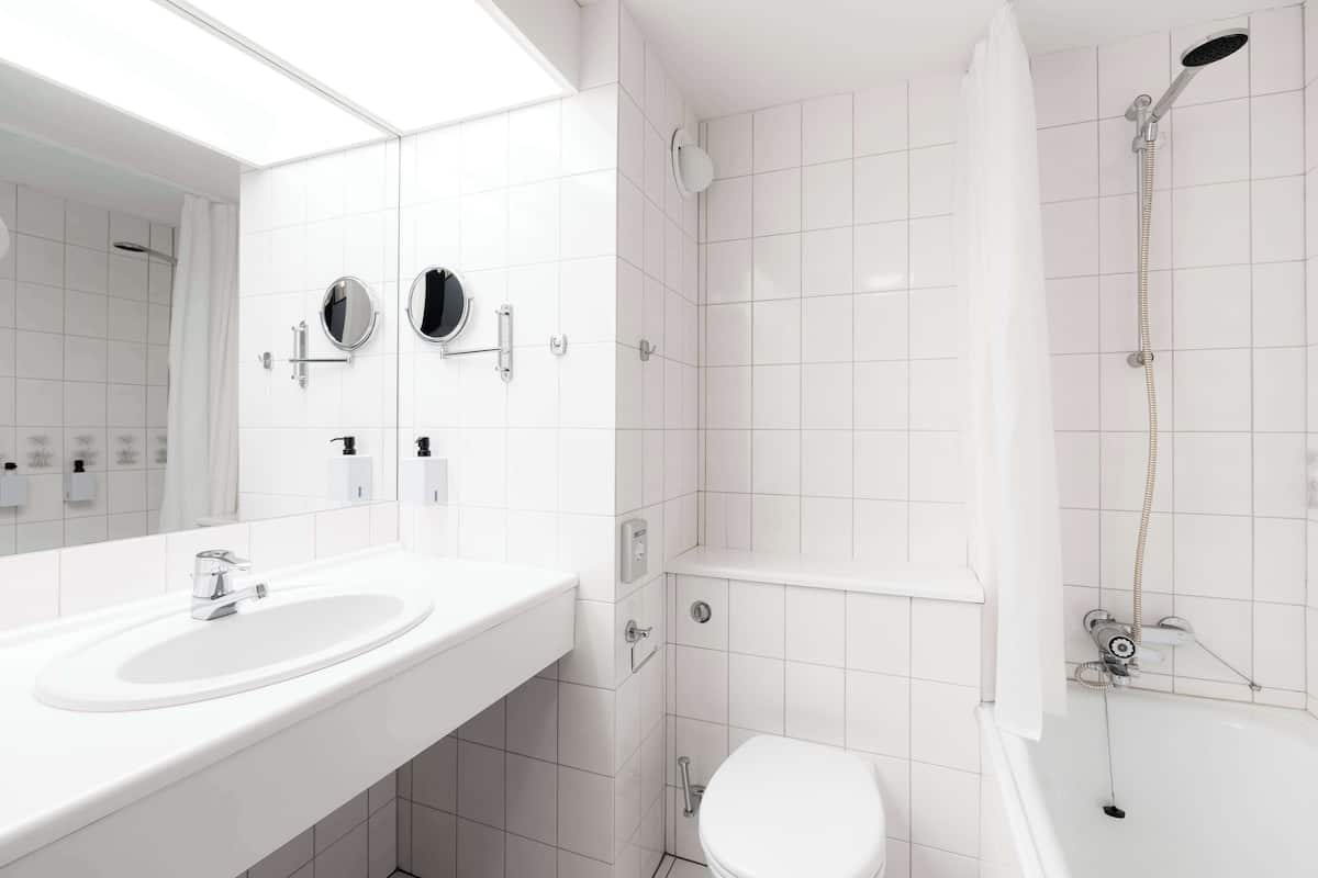 A modern bathroom with a white sink, two mirrors, a toilet, and a shower.