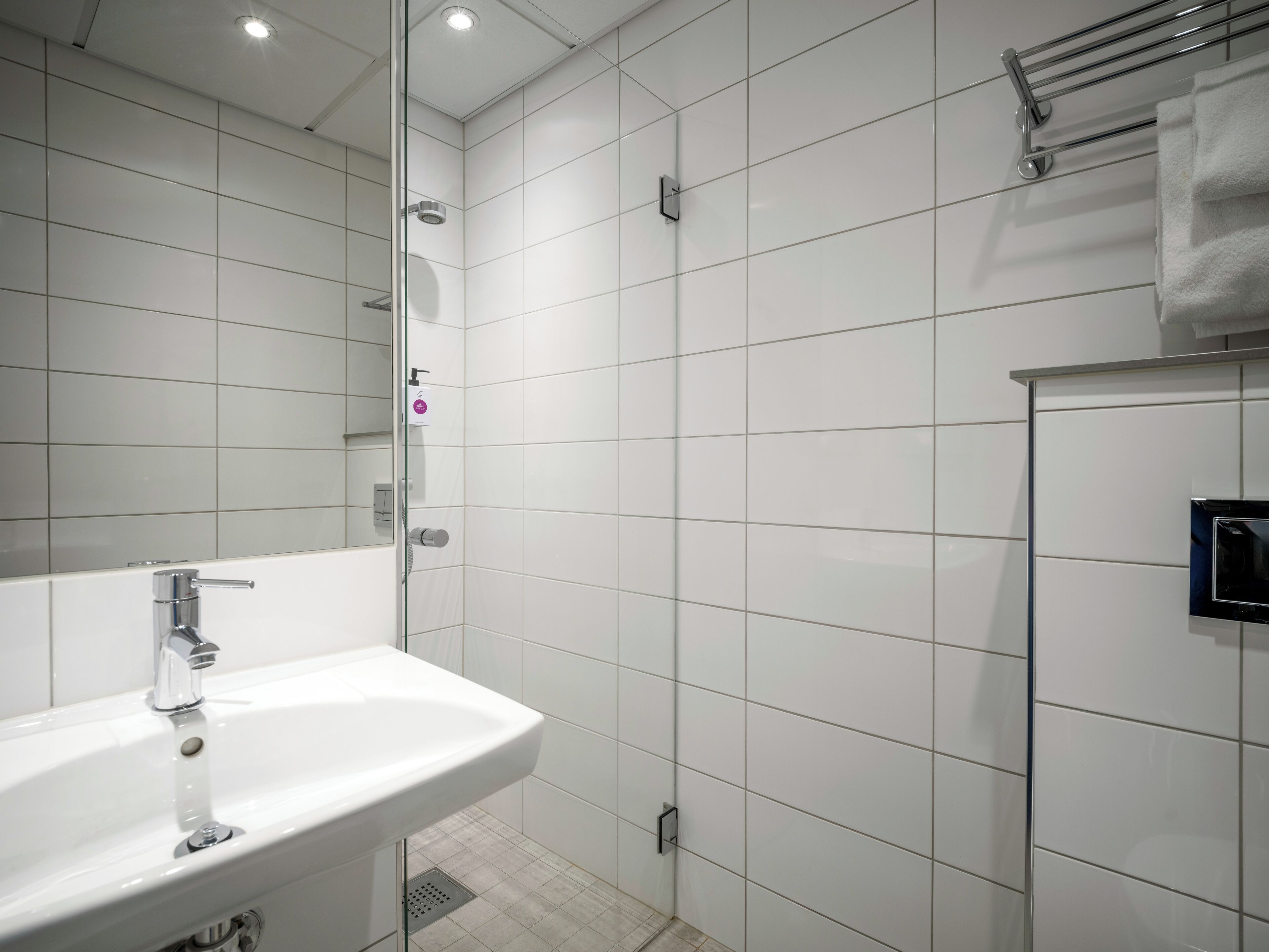 A modern bathroom with a white sink, a glass shower enclosure, and a towel rack.