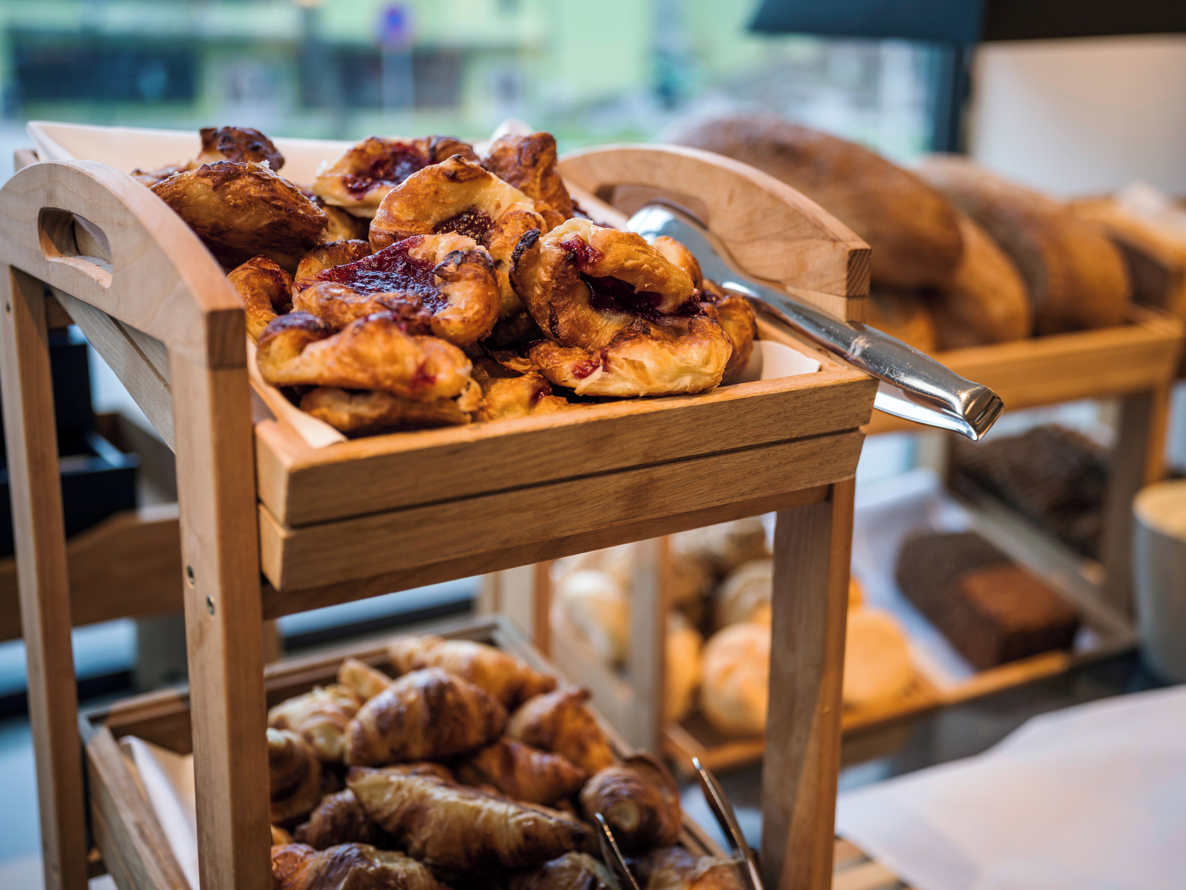 A wooden serving cart with pastries and bread.