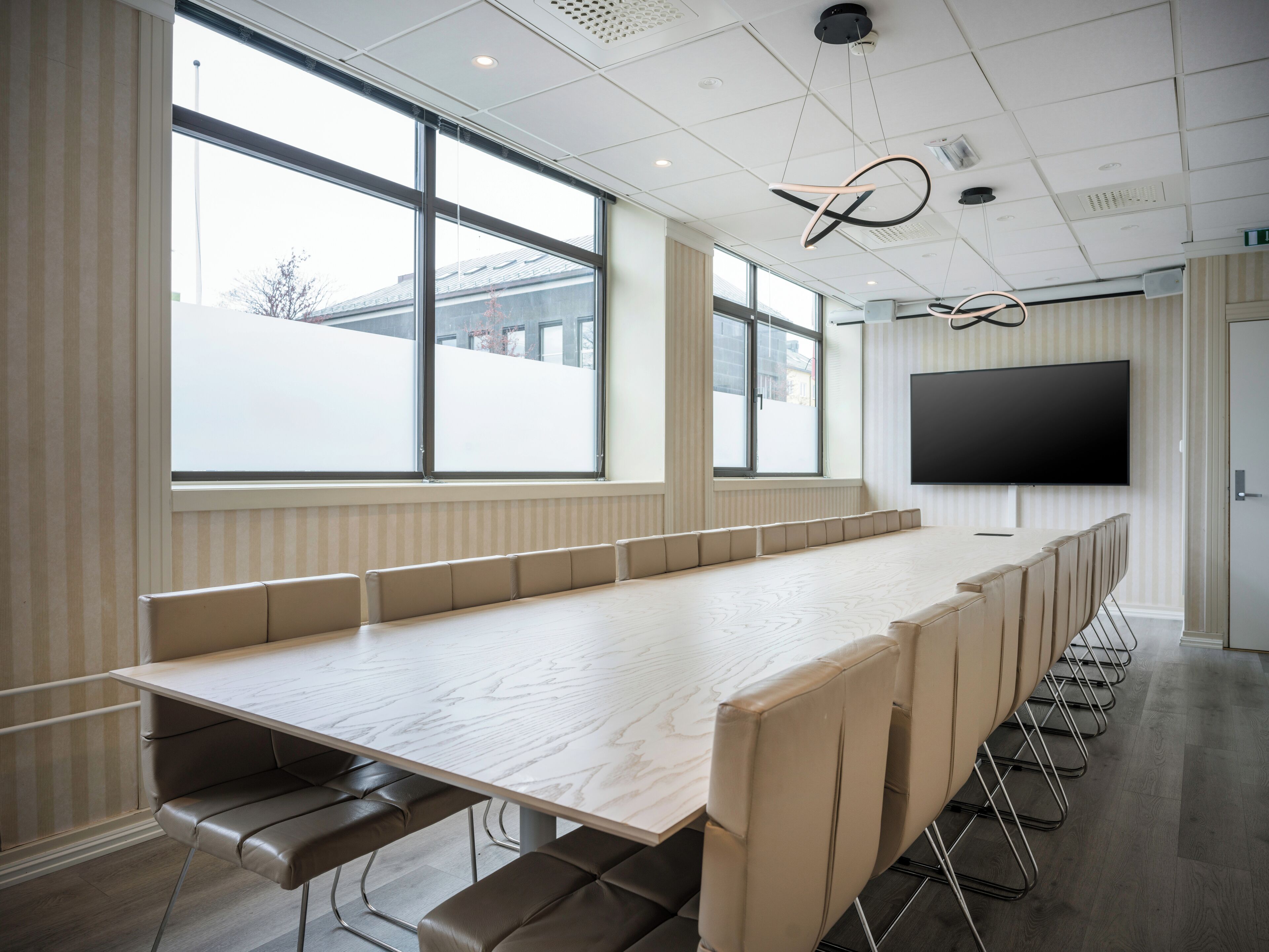 A conference room with a long table, cushioned benches, large windows, and a mounted TV.