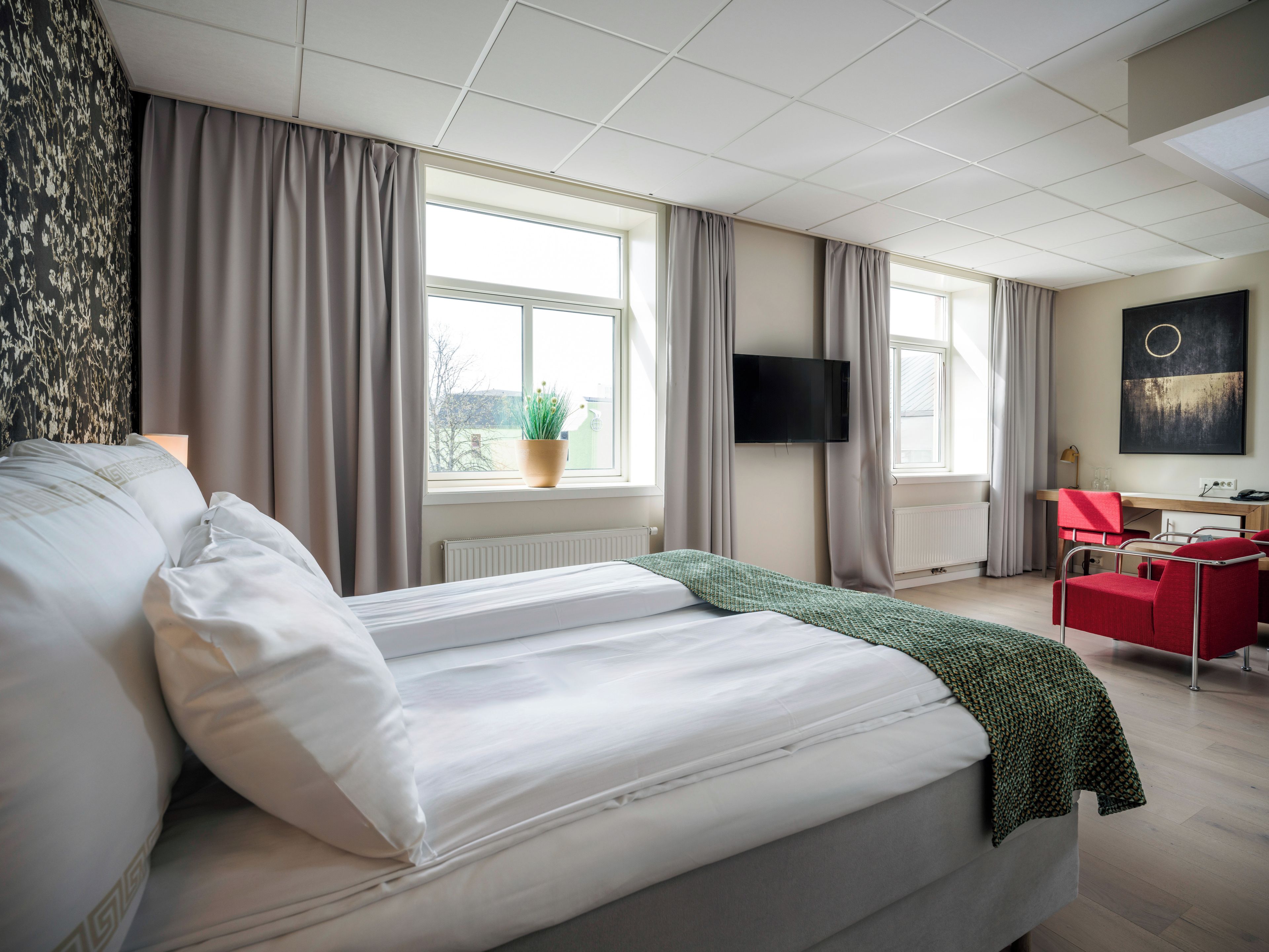 Quarto de hotel com cama, escrivaninha, cadeira, televisão e janela com cortinas.