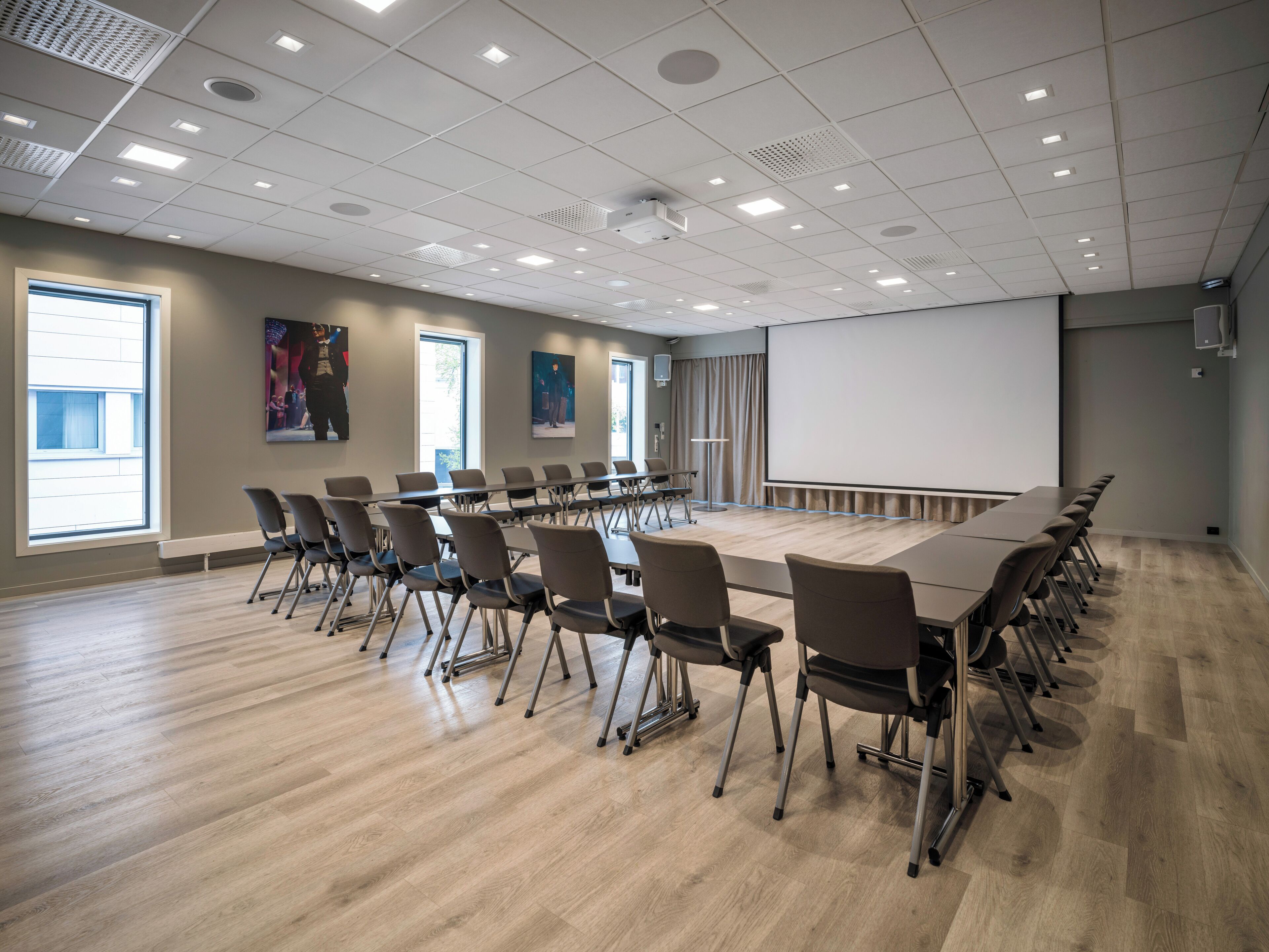 A conference room with a long table, chairs, a projector screen, and large windows.