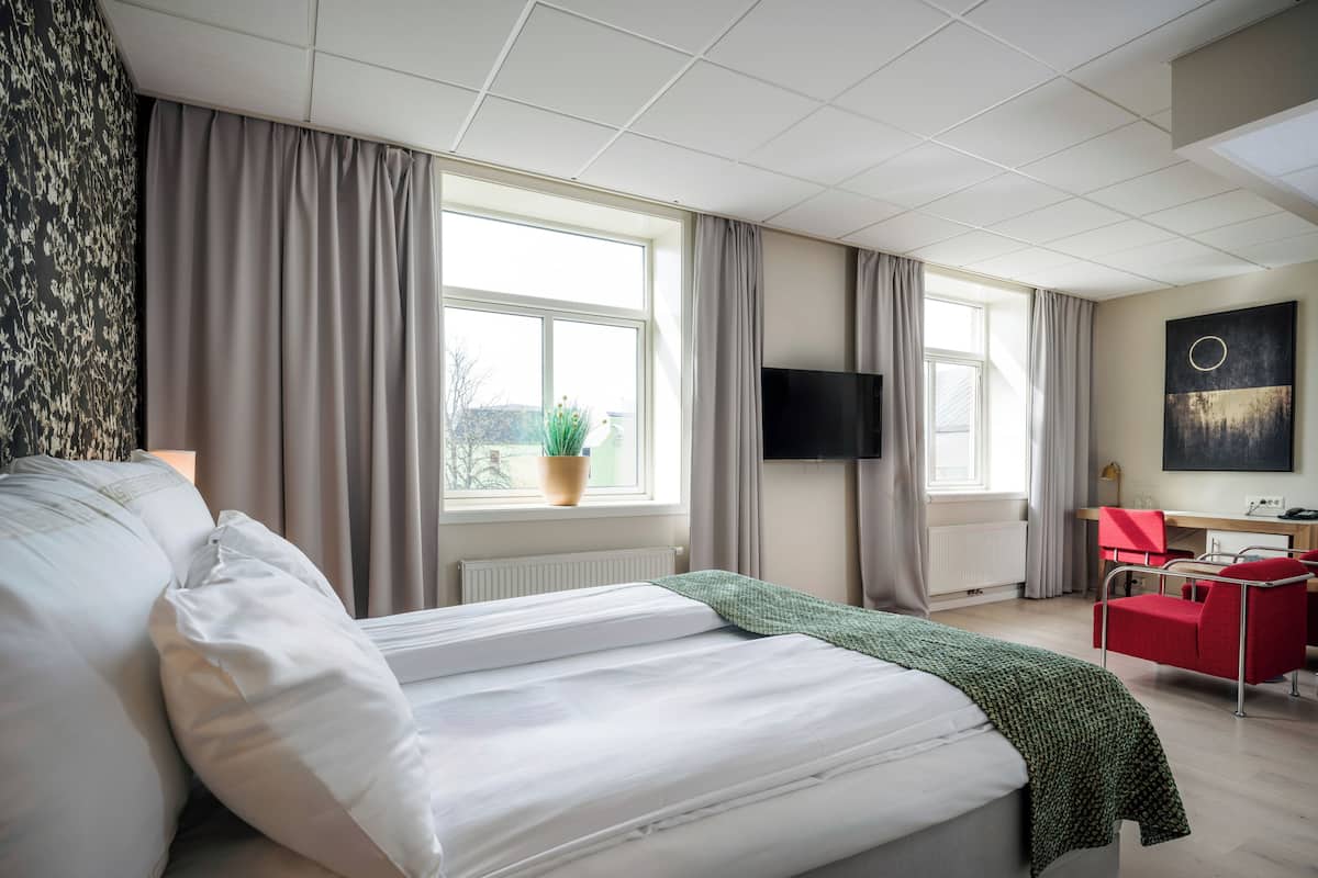 Une chambre d’hôtel avec un lit, un bureau, une chaise, une télévision et une fenêtre avec des rideaux.