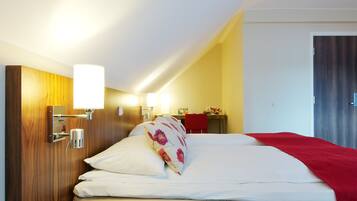 A hotel room with a wooden headboard, a bed with white bedding and a red blanket, a bedside table, and a wall-mounted lamp.