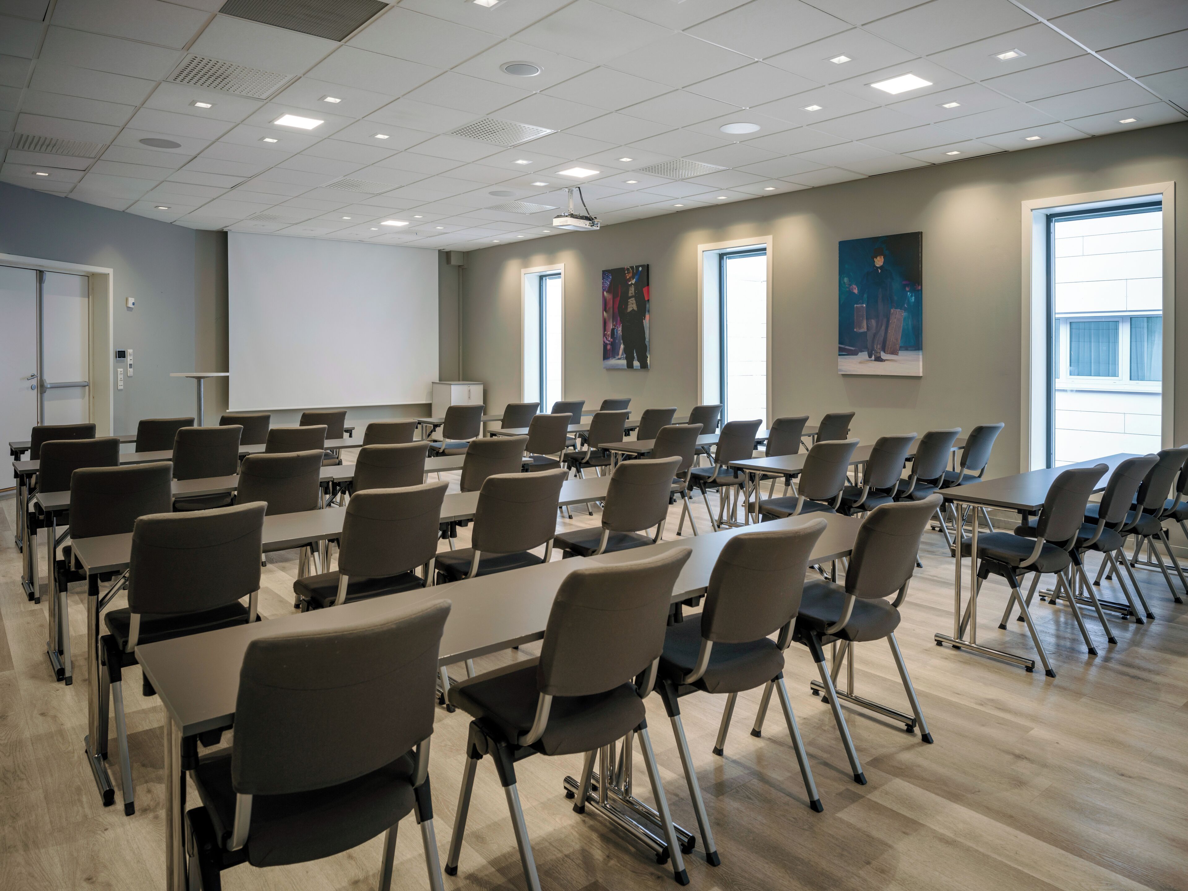 A conference room with rows of tables and chairs, a projector screen, and large windows.