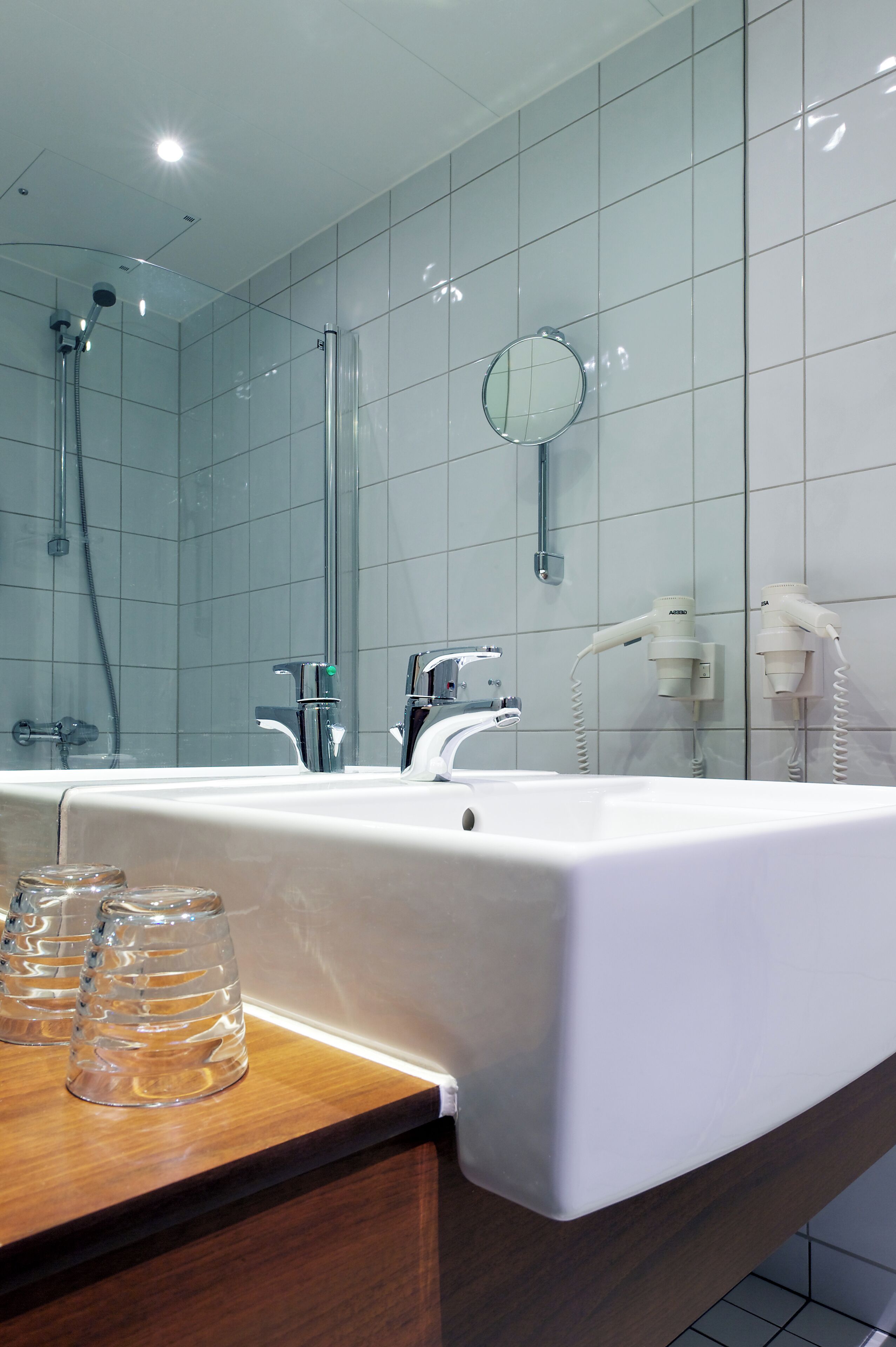 Een moderne badkamer met een grote spiegel, een witte wastafel en een douchehoek.