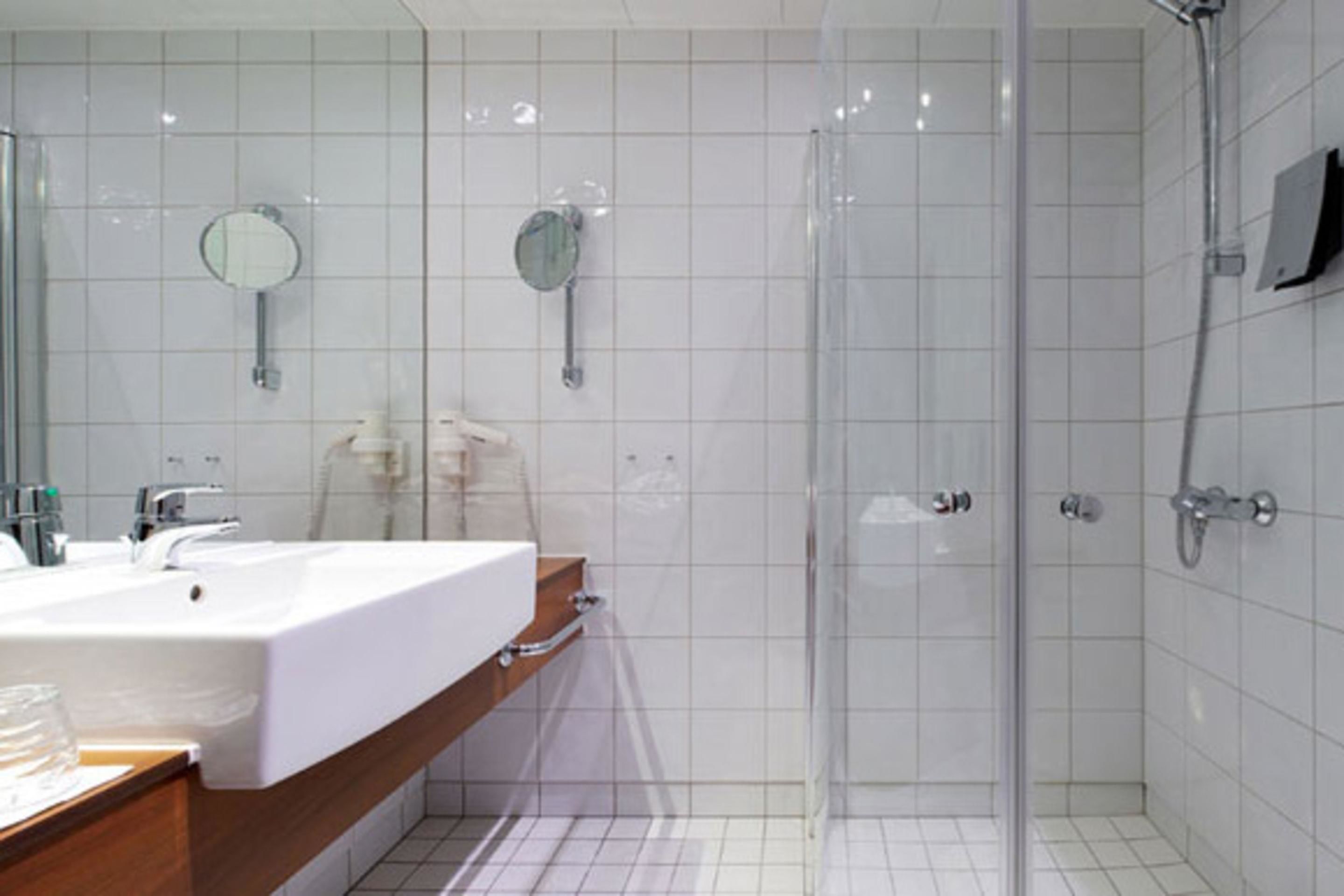 Un baño moderno con un lavamanos grande de color blanco, un espejo y una zona de ducha con paredes de vidrio.