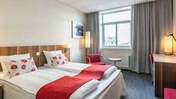 Una habitación de hotel con una cama grande, dos mesitas de noche, una silla, un escritorio y una ventana con cortinas.