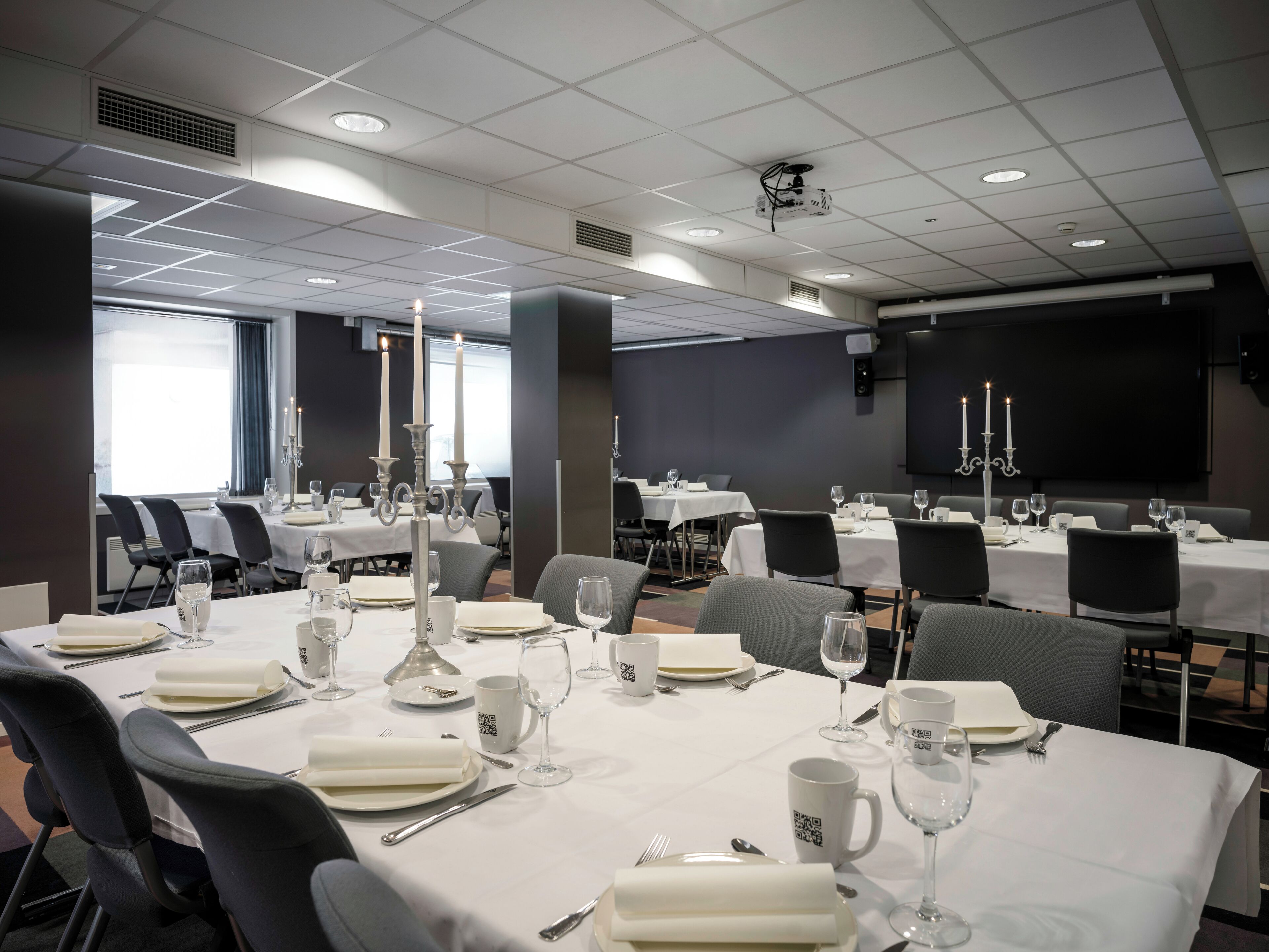 A conference room with tables set for a meeting, equipped with projectors and screens.
