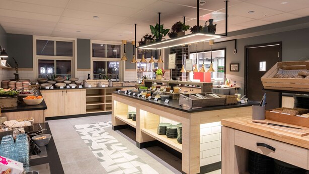 Un restaurante moderno con barra tipo buffet, mostrador de madera y plantas colgantes.