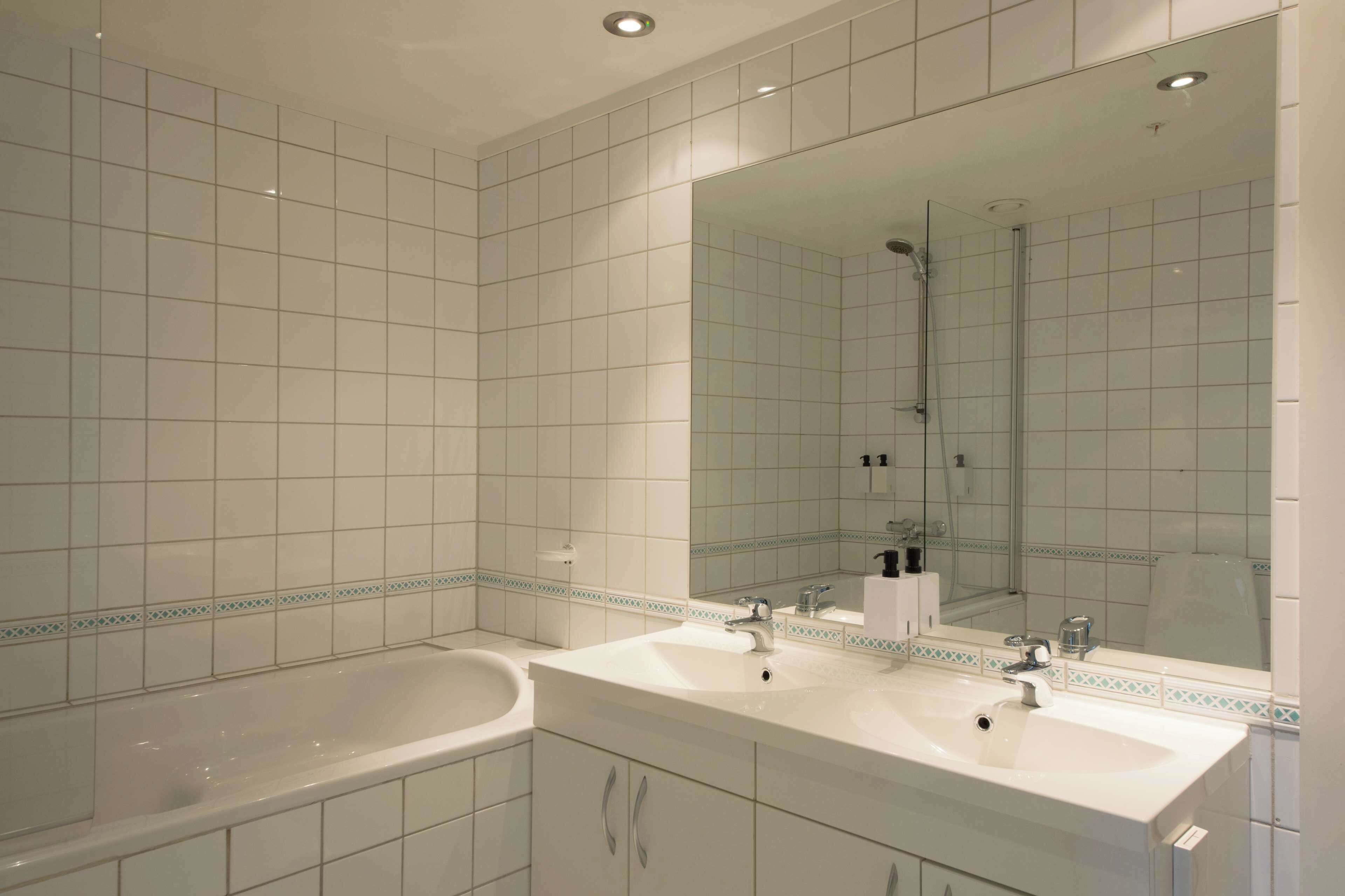 Een moderne badkamer met twee wastafels, een bad en een grote spiegel.